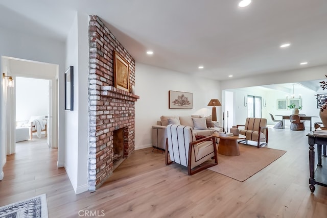 living room featuring recessed lighting, light wood-type flooring, a brick fireplace, and an inviting chandelier