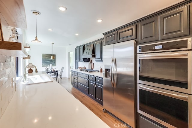 kitchen featuring a sink, decorative backsplash, light countertops, custom range hood, and stainless steel appliances