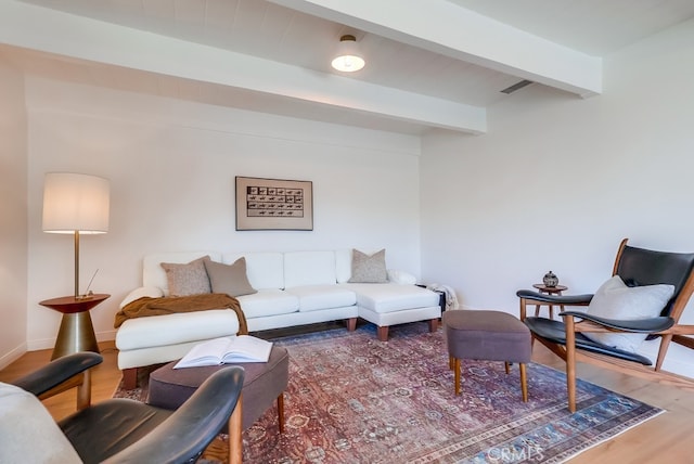 living room featuring beam ceiling, visible vents, baseboards, and wood finished floors