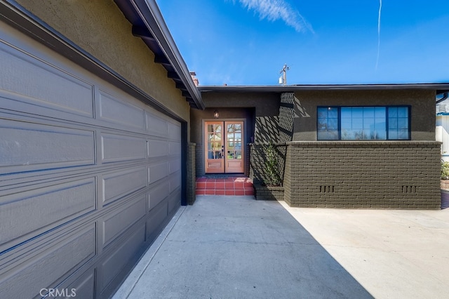 view of exterior entry with brick siding, stucco siding, driveway, crawl space, and an attached garage