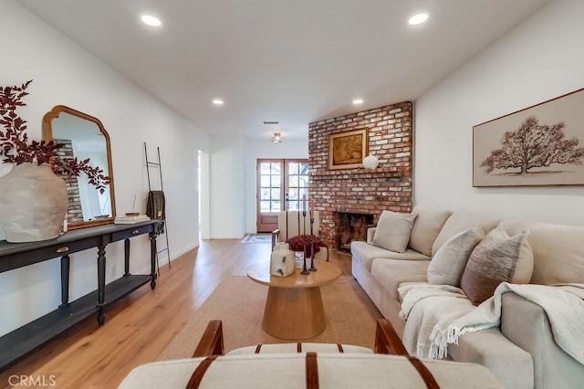 living area featuring a brick fireplace, light wood-style flooring, recessed lighting, and french doors