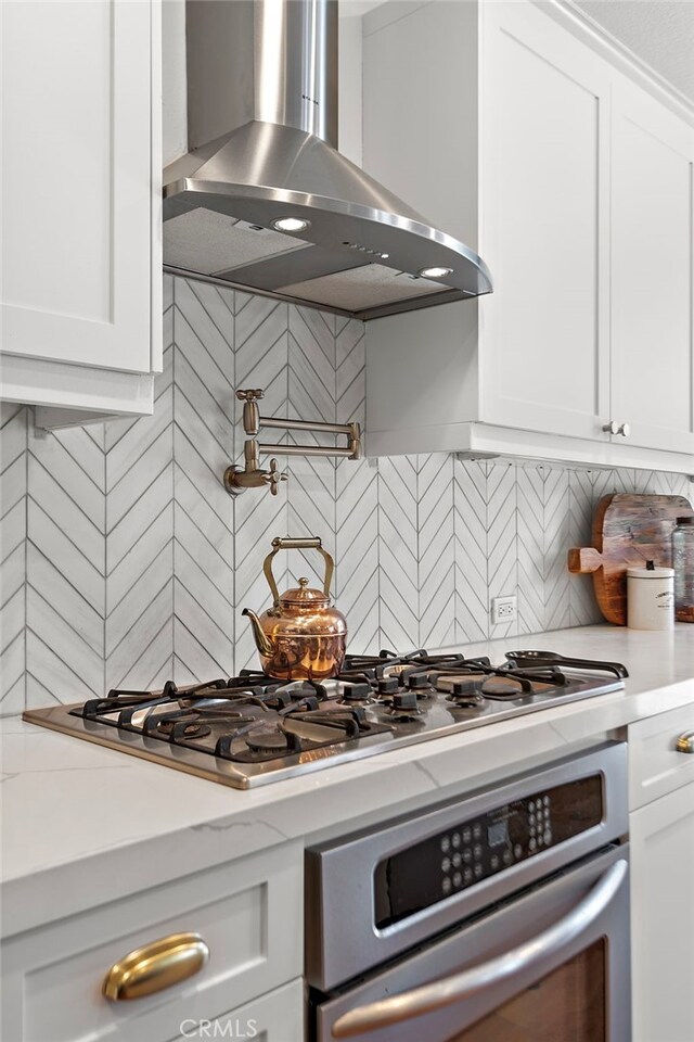 kitchen with oven, wall chimney range hood, light stone counters, decorative backsplash, and white cabinets