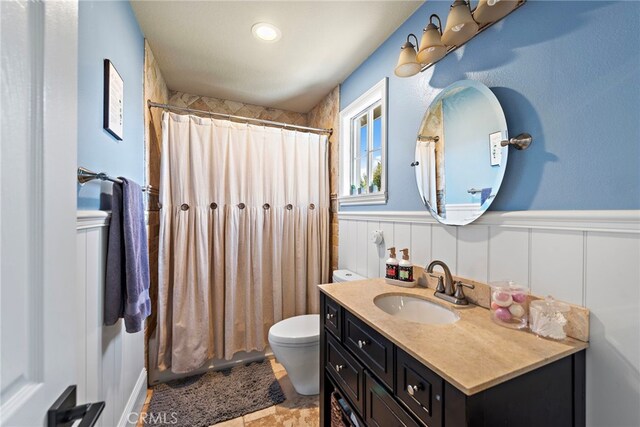 bathroom with a shower with curtain, vanity, toilet, and wainscoting