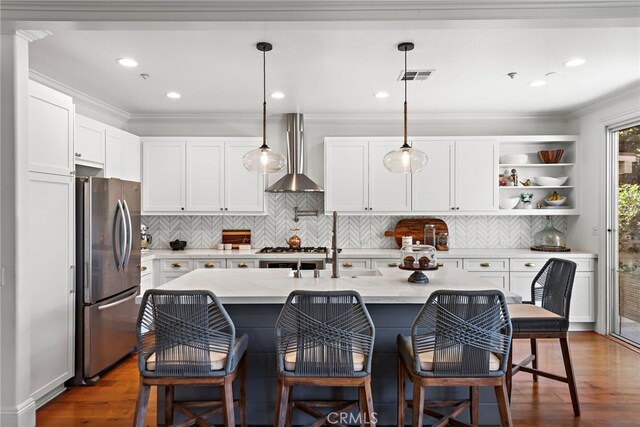 kitchen featuring visible vents, wall chimney range hood, freestanding refrigerator, dark wood-style floors, and white cabinetry