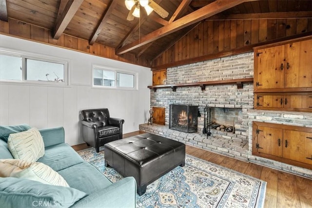 living area featuring wood finished floors, wooden ceiling, a brick fireplace, ceiling fan, and vaulted ceiling with beams