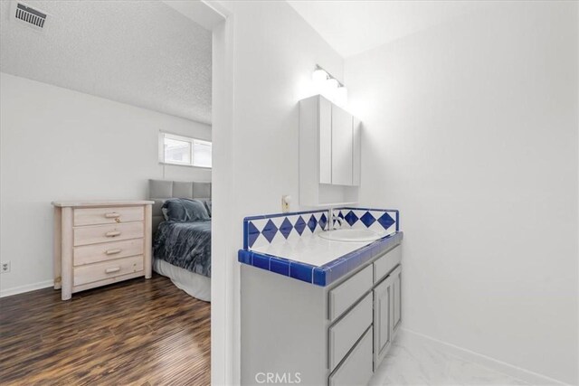 bathroom with visible vents, a textured ceiling, wood finished floors, baseboards, and vanity