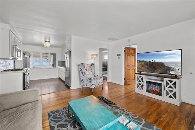 living room with arched walkways, visible vents, baseboards, and dark wood-style flooring