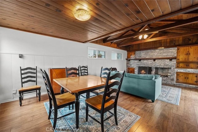 dining room featuring light wood finished floors, a fireplace, wooden ceiling, and lofted ceiling