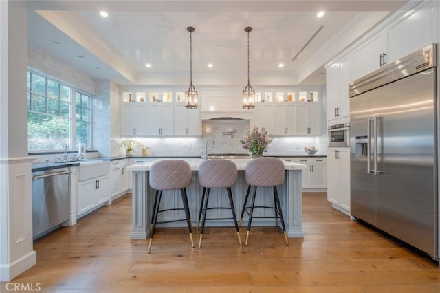 kitchen featuring a raised ceiling, stainless steel appliances, crown molding, and light wood-type flooring