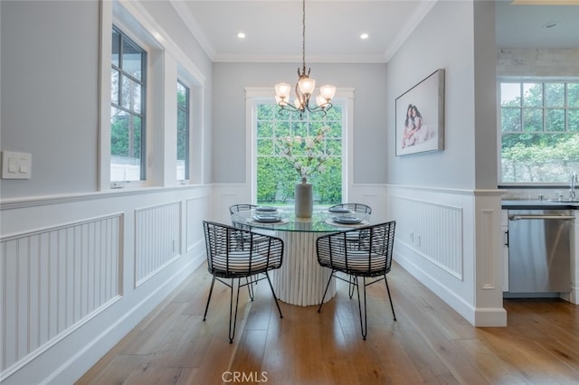 dining space with light wood-style flooring, a wainscoted wall, an inviting chandelier, and ornamental molding