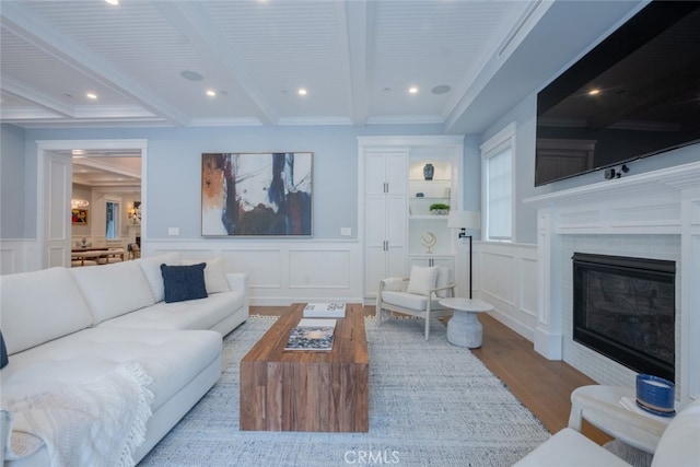 living area featuring a decorative wall, wood finished floors, a glass covered fireplace, and beam ceiling