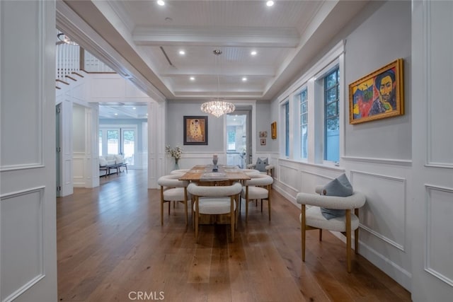 dining room featuring crown molding, wood-type flooring, beamed ceiling, a decorative wall, and a notable chandelier