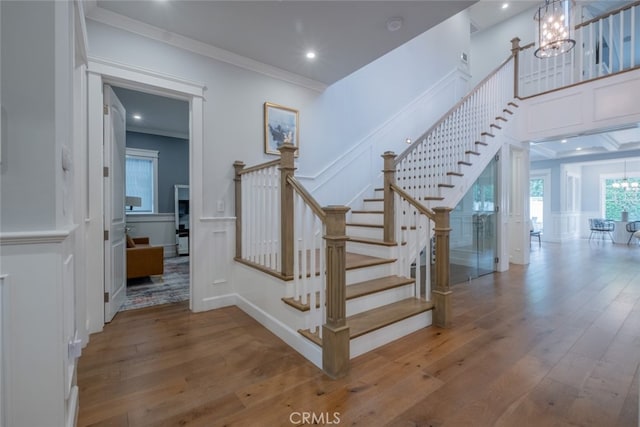 stairs with a wainscoted wall, ornamental molding, wood-type flooring, a decorative wall, and a chandelier