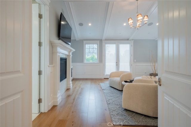 living area with a decorative wall, a wainscoted wall, beam ceiling, light wood-style floors, and a glass covered fireplace