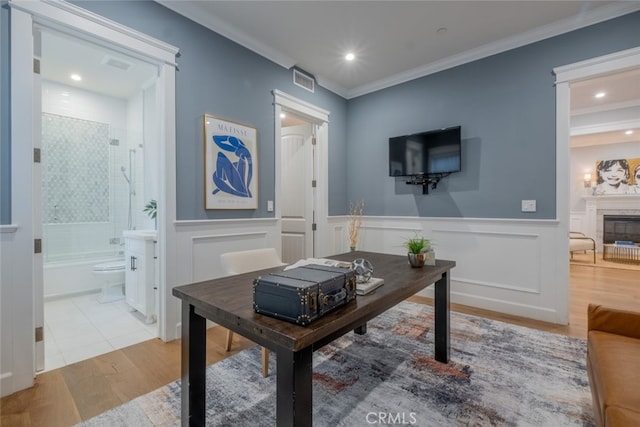 office area featuring crown molding, wood finished floors, a glass covered fireplace, wainscoting, and visible vents