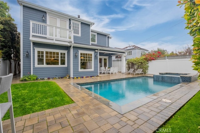 back of property with a lawn, a pool with connected hot tub, a patio, a fenced backyard, and a balcony