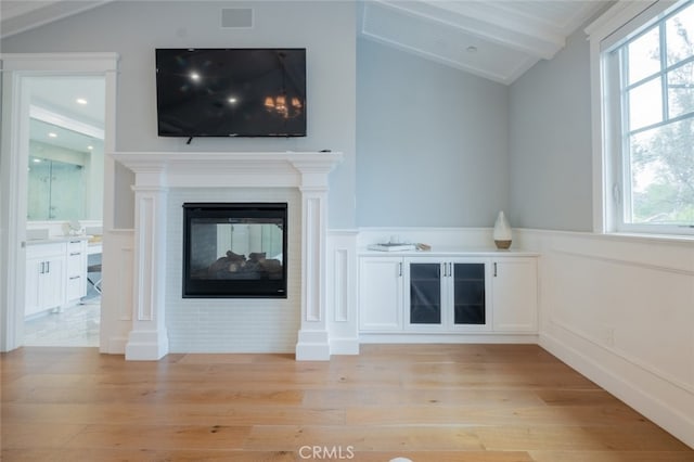 unfurnished living room with lofted ceiling with beams, light wood-type flooring, a multi sided fireplace, and visible vents