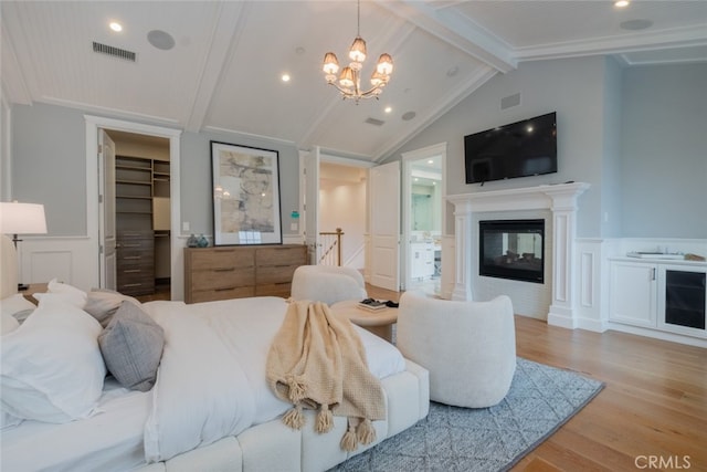 bedroom featuring visible vents, wainscoting, lofted ceiling with beams, and wood finished floors