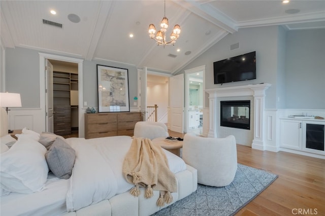 bedroom featuring a wainscoted wall, lofted ceiling with beams, wood finished floors, and an inviting chandelier