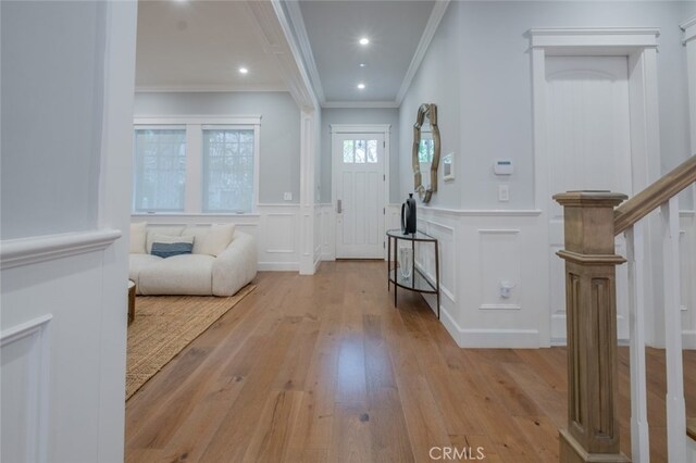 foyer with crown molding, light wood-style flooring, recessed lighting, a wainscoted wall, and a decorative wall