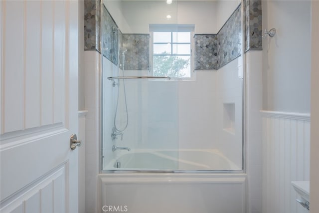 full bath with combined bath / shower with glass door and a wainscoted wall