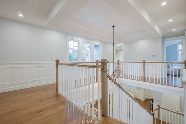 corridor with an upstairs landing, a decorative wall, wood finished floors, recessed lighting, and a raised ceiling