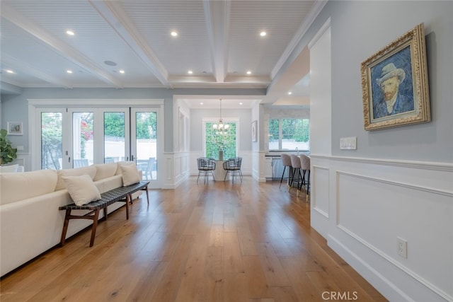 living room featuring a decorative wall, beamed ceiling, a chandelier, and light wood-type flooring