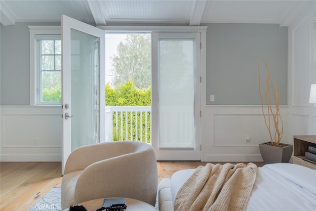 bedroom with a wainscoted wall, access to exterior, light wood finished floors, a decorative wall, and beamed ceiling