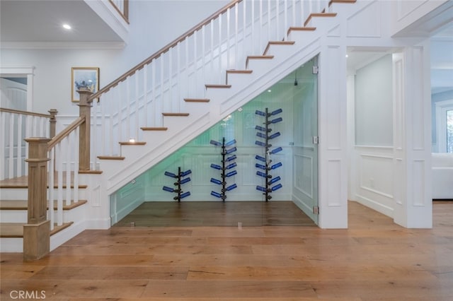 stairway with a decorative wall, wood finished floors, a towering ceiling, and ornamental molding