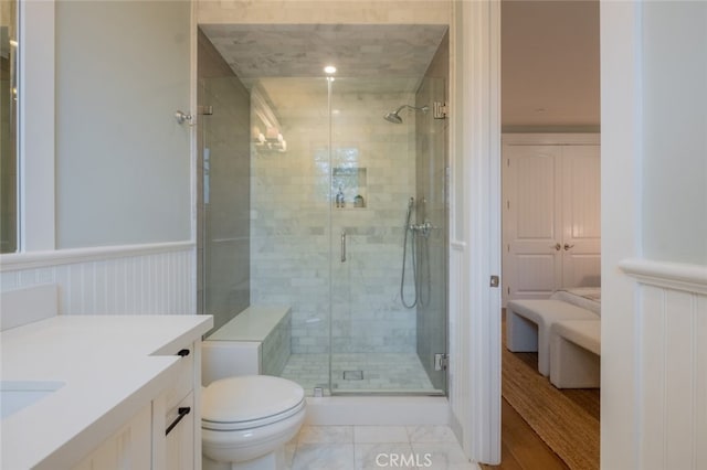 full bath featuring toilet, vanity, a shower stall, and wainscoting