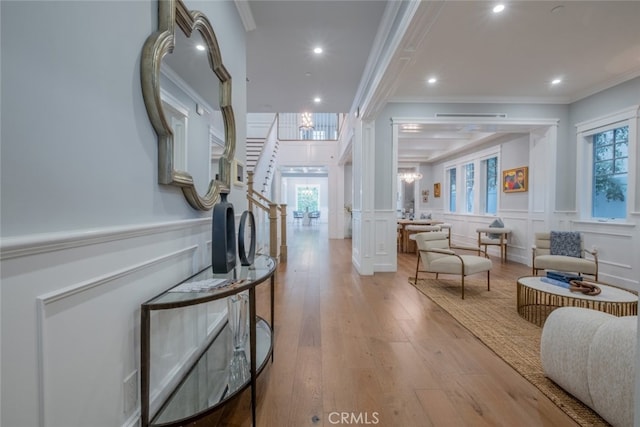 hall with crown molding, light wood-style floors, a wealth of natural light, a decorative wall, and wainscoting