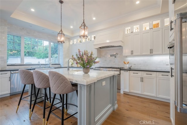 kitchen with custom exhaust hood, light wood-type flooring, and a raised ceiling