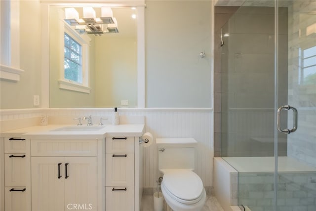 bathroom featuring toilet, vanity, a stall shower, and wainscoting
