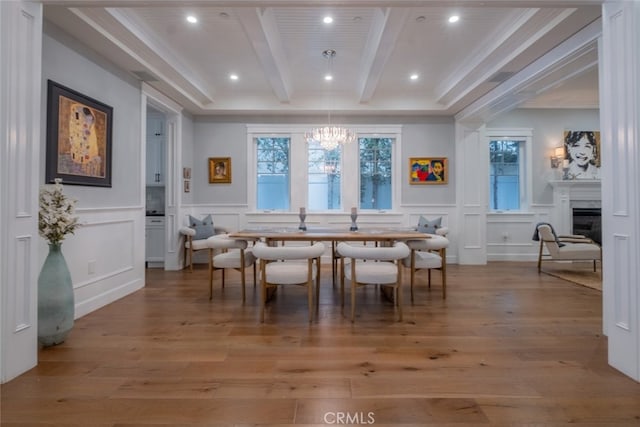 dining area with an inviting chandelier, beam ceiling, light wood-style flooring, a fireplace, and a decorative wall