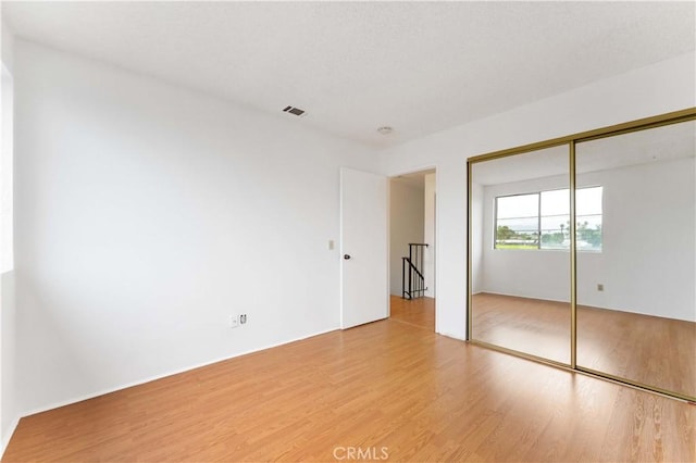 unfurnished bedroom with a closet, visible vents, a textured ceiling, and wood finished floors