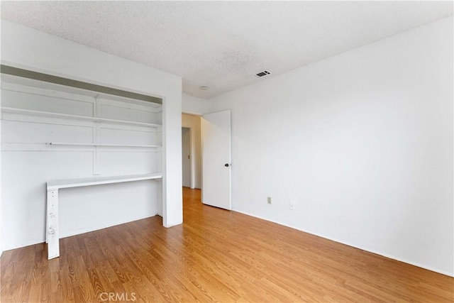 interior space featuring a closet, visible vents, a textured ceiling, and wood finished floors