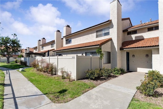 exterior space featuring a tiled roof, stucco siding, a chimney, and fence