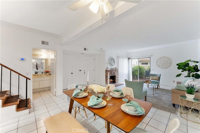 dining space with visible vents, a ceiling fan, a fireplace, light tile patterned floors, and stairs