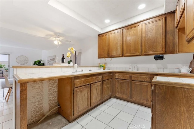 kitchen with a sink, tile countertops, a peninsula, and brown cabinetry