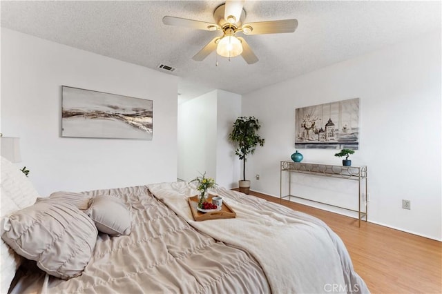 bedroom featuring visible vents, a textured ceiling, ceiling fan, and wood finished floors