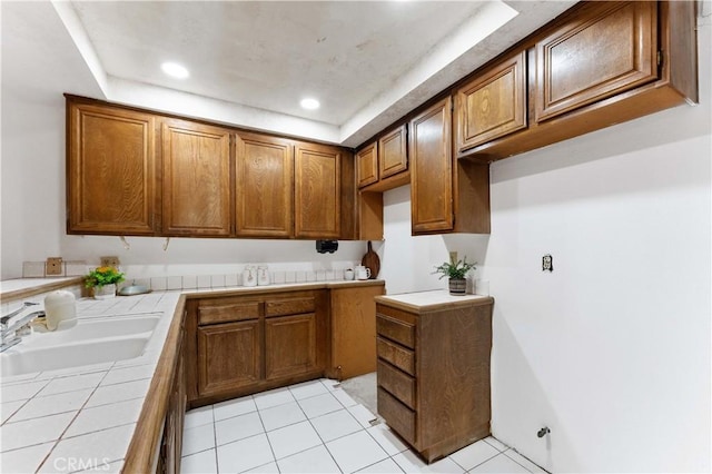 kitchen with tile counters, light tile patterned floors, recessed lighting, brown cabinetry, and a sink