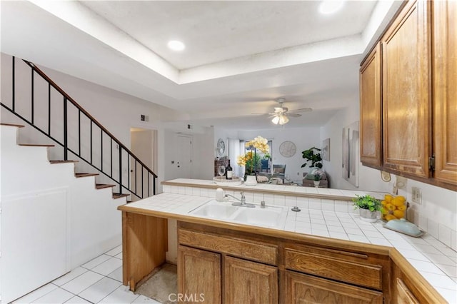 kitchen featuring a sink, a peninsula, brown cabinetry, light tile patterned floors, and tile counters