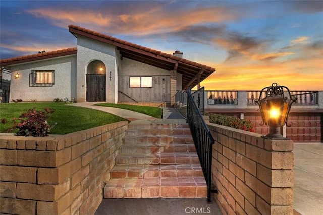 view of front of home with stucco siding, a tile roof, stairs, and a front yard