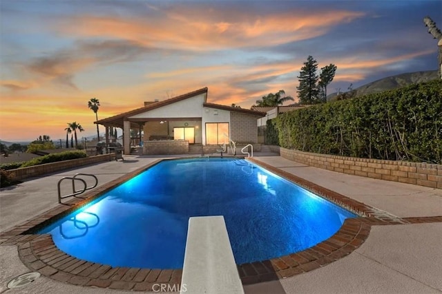 pool at dusk with a diving board, a fenced in pool, and a patio