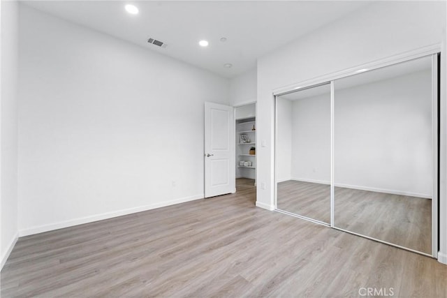 unfurnished bedroom featuring wood finished floors, visible vents, baseboards, recessed lighting, and a closet