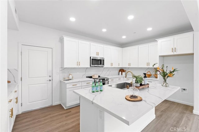 kitchen featuring a sink, appliances with stainless steel finishes, white cabinets, light wood finished floors, and light stone countertops