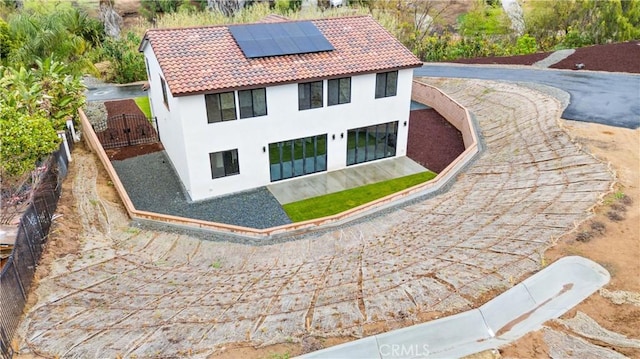 exterior space featuring fence, a tiled roof, roof mounted solar panels, stucco siding, and a gate