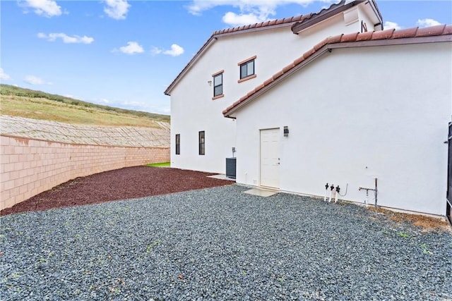 view of side of home featuring central AC unit, fence, stucco siding, a tile roof, and a patio area