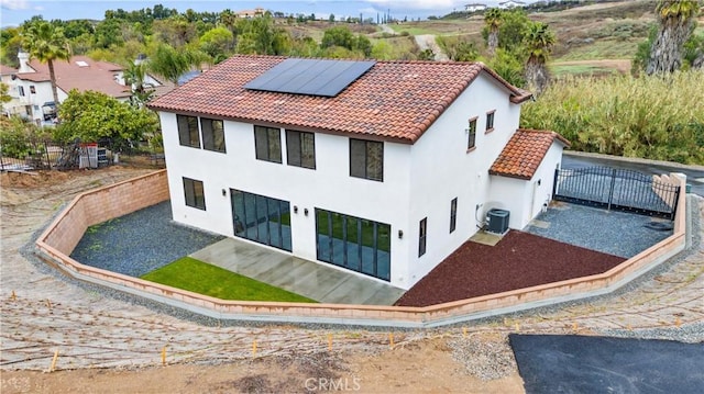 view of home's exterior with central AC unit, a fenced backyard, stucco siding, a tiled roof, and roof mounted solar panels