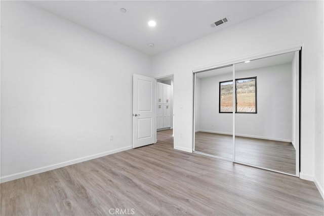 unfurnished bedroom featuring wood finished floors, visible vents, a closet, and baseboards